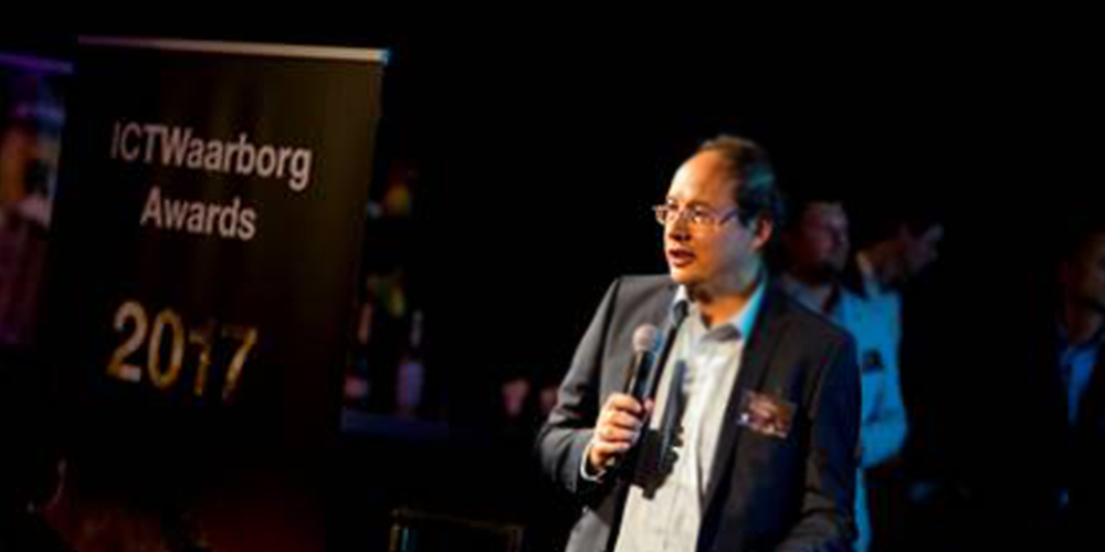 Man in a suit and glasses presenting at an awards ceremony