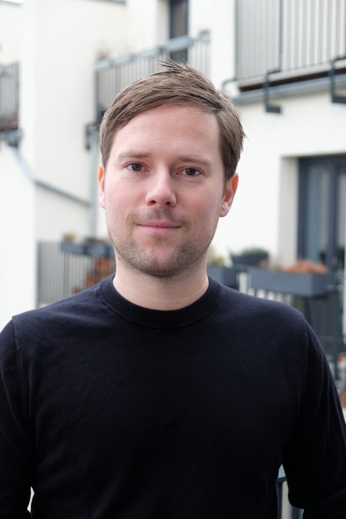 A man with brown hair, wearing a black shirt, posing for a photo