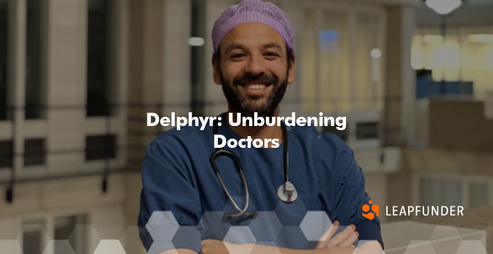 A doctor with a beard, wearing a blue shirt and a stethoscope, posing for a photo 